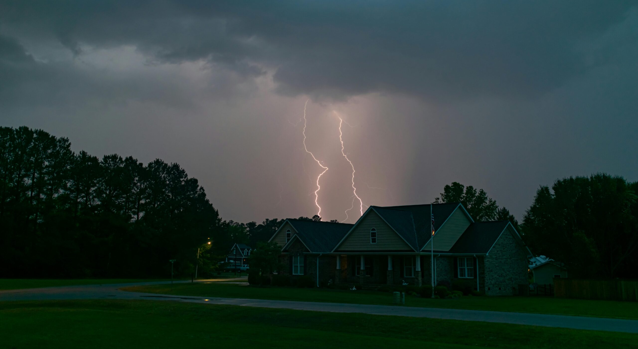 A powerful lightning bolt illuminates a suburban neighborhood under an overcast sky.
